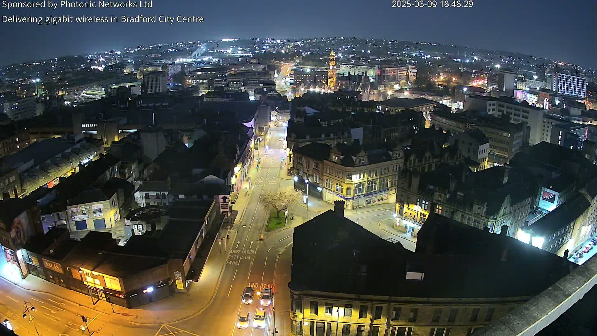 A nighttime aerial view of a city center with illuminated streets and buildings under a clear sky.
