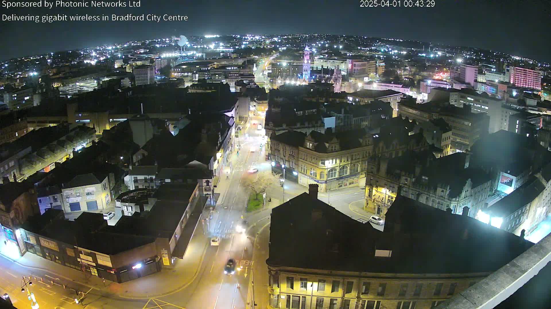 A nighttime aerial view of a city center with illuminated buildings and streets showing minimal traffic.