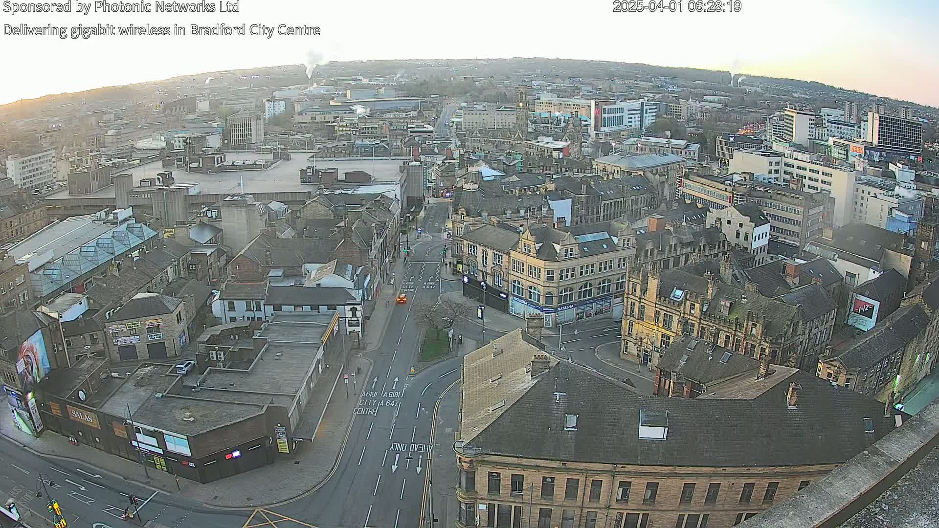 A high-angle, long shot of a city center at dawn, showing many buildings and streets, with a clear sky.