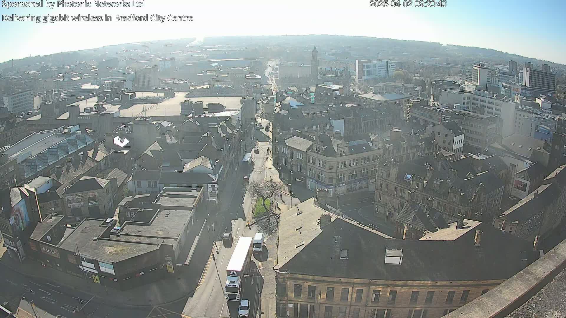 A high-angle, long shot of a city center on a hazy, sunny day, showing a network of streets and buildings.