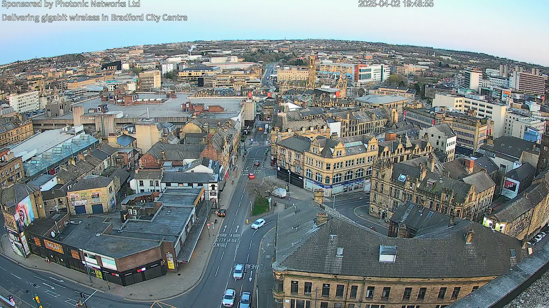 A high-angle, wide shot of a city center at dusk, showing many buildings and streets with sparse traffic.
