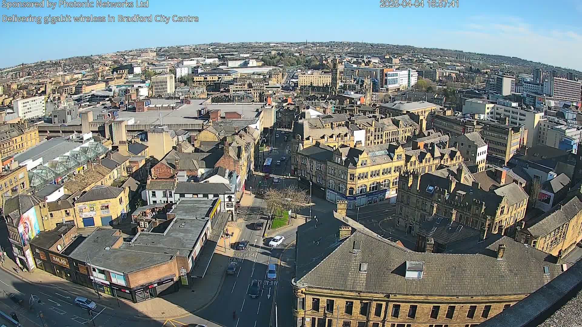A high-angle, sunny view of a city center, showing numerous buildings, streets, and a few vehicles.