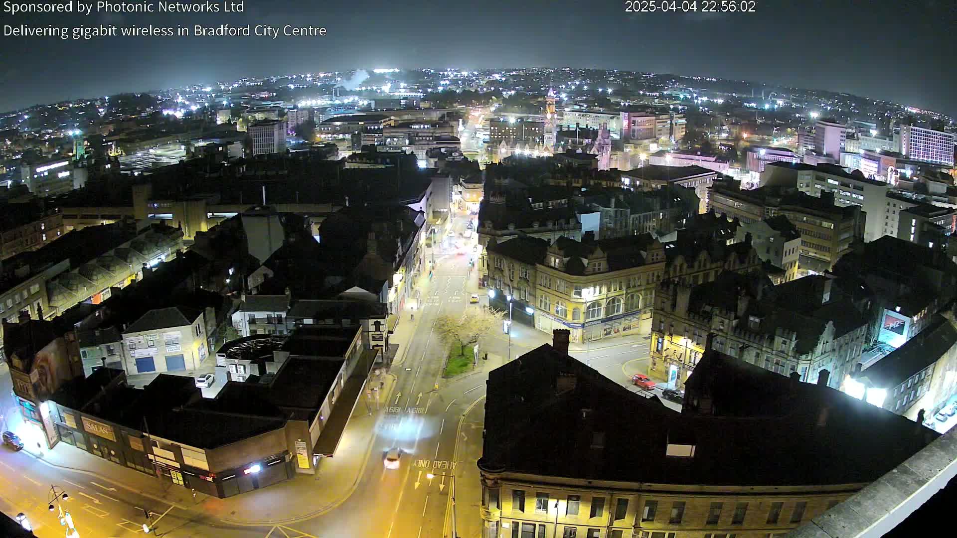 A nighttime, high-angle view of a city center with illuminated buildings and streets, showing minimal vehicle traffic.