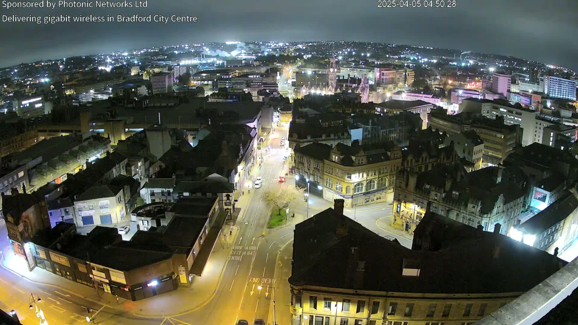 A nighttime aerial view of a city center, showing illuminated streets and buildings under a dark sky.