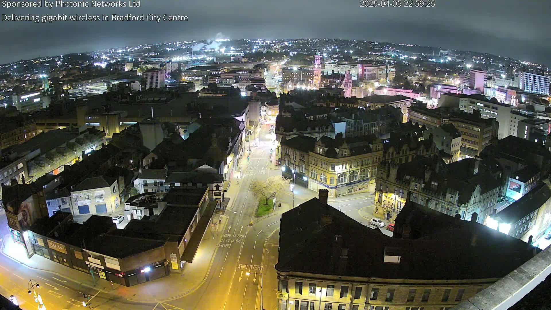 A nighttime aerial view of a city center, showing illuminated streets and buildings under a clear sky.