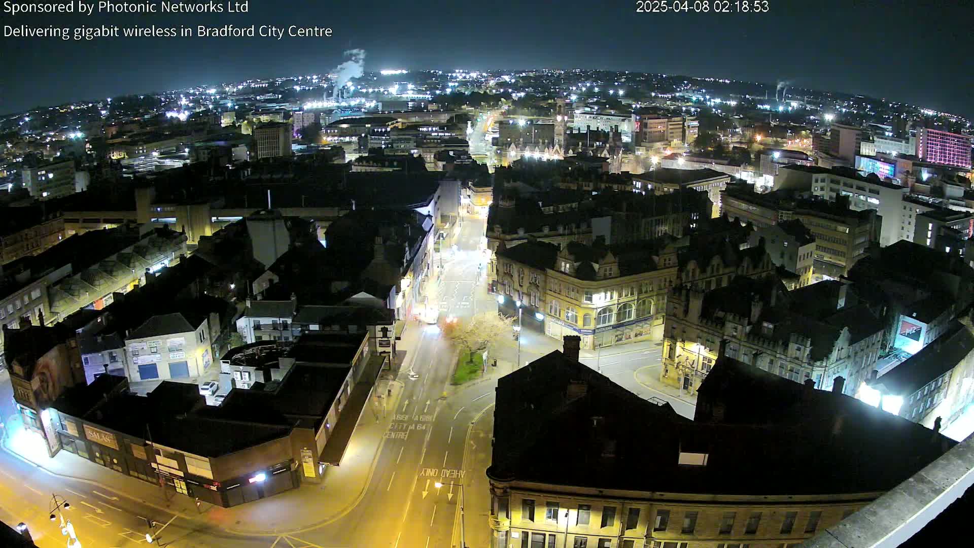 A nighttime, high-angle view of a city center with illuminated streets and buildings under a clear, dark sky.