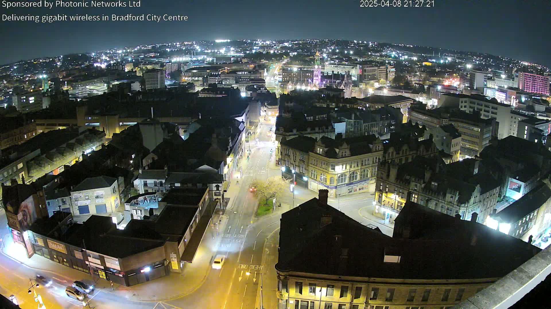 A nighttime aerial view of a city center, showing illuminated streets and buildings under a clear sky.