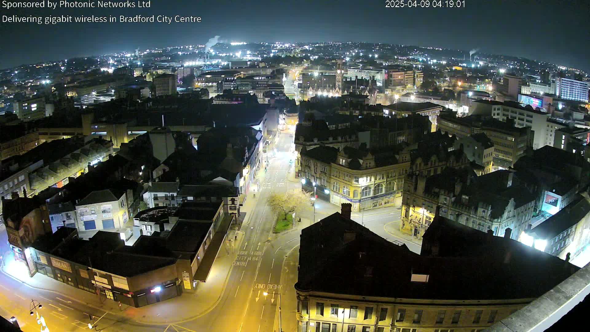 A nighttime aerial view of a city center with illuminated streets and buildings under a clear sky.