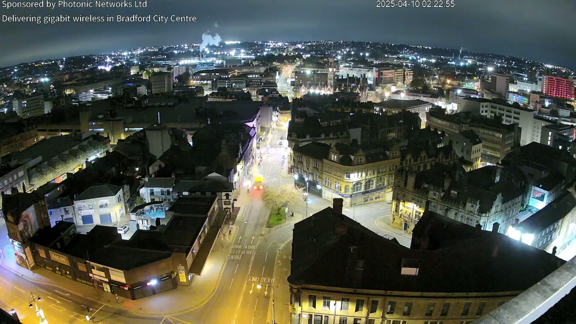 A nighttime, high-angle view of a city center, showing illuminated streets and buildings under a clear sky.