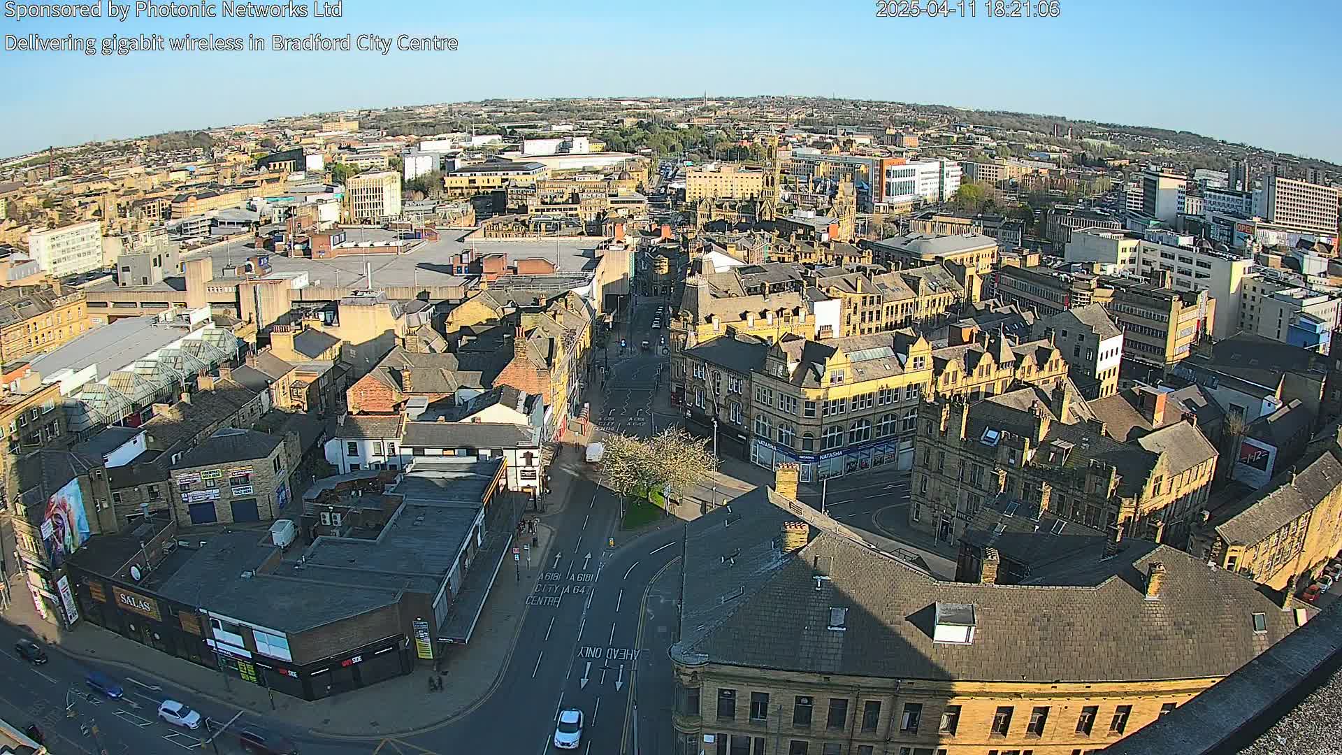 A high-angle, long shot of a city on a sunny day, showing many brownstone buildings and roadways.