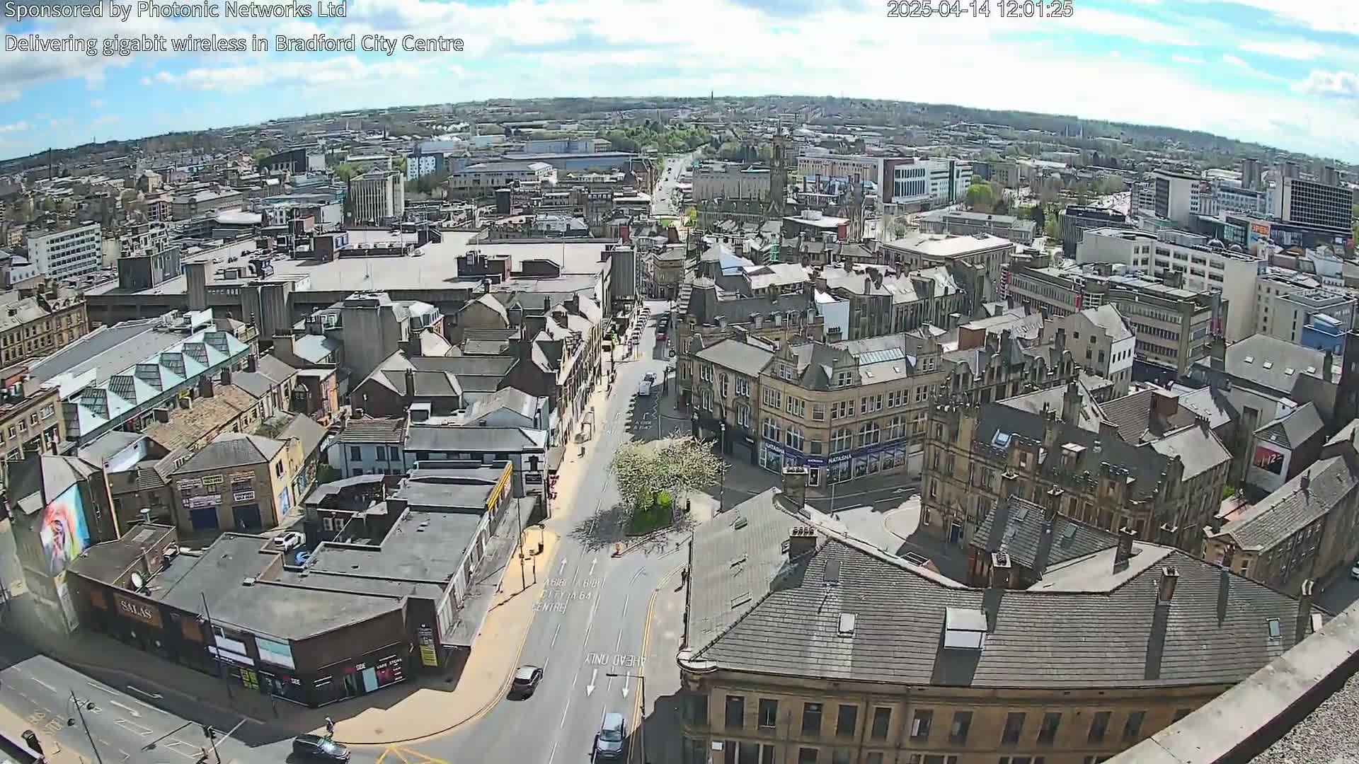 A high-angle, sunny view of a city center with many buildings and a few cars on the streets.