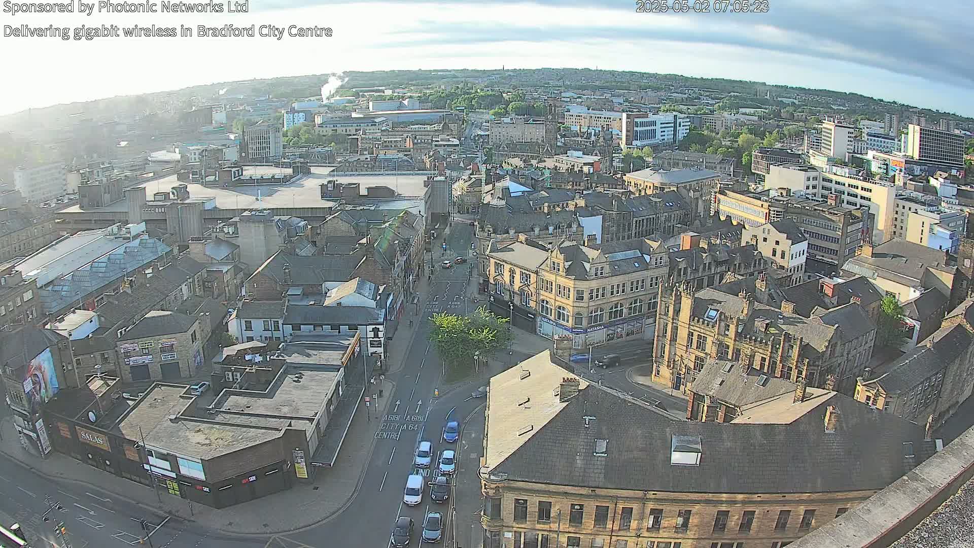A high-angle, long shot of a city center on a partly cloudy day, showing numerous buildings and vehicles on streets below.