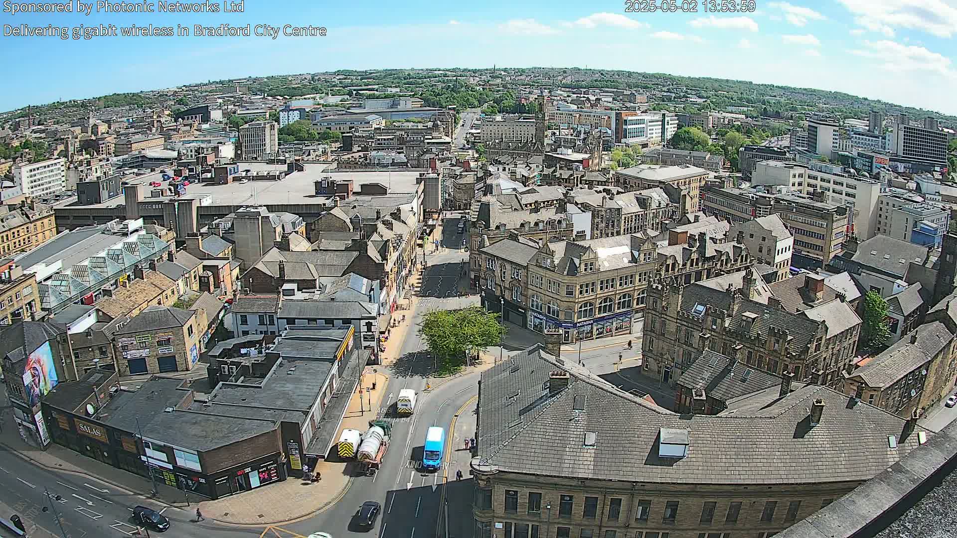 A high-angle, sunny-day view of a city's dense, historic center with many brownstone buildings, intersecting streets, and some vehicles.