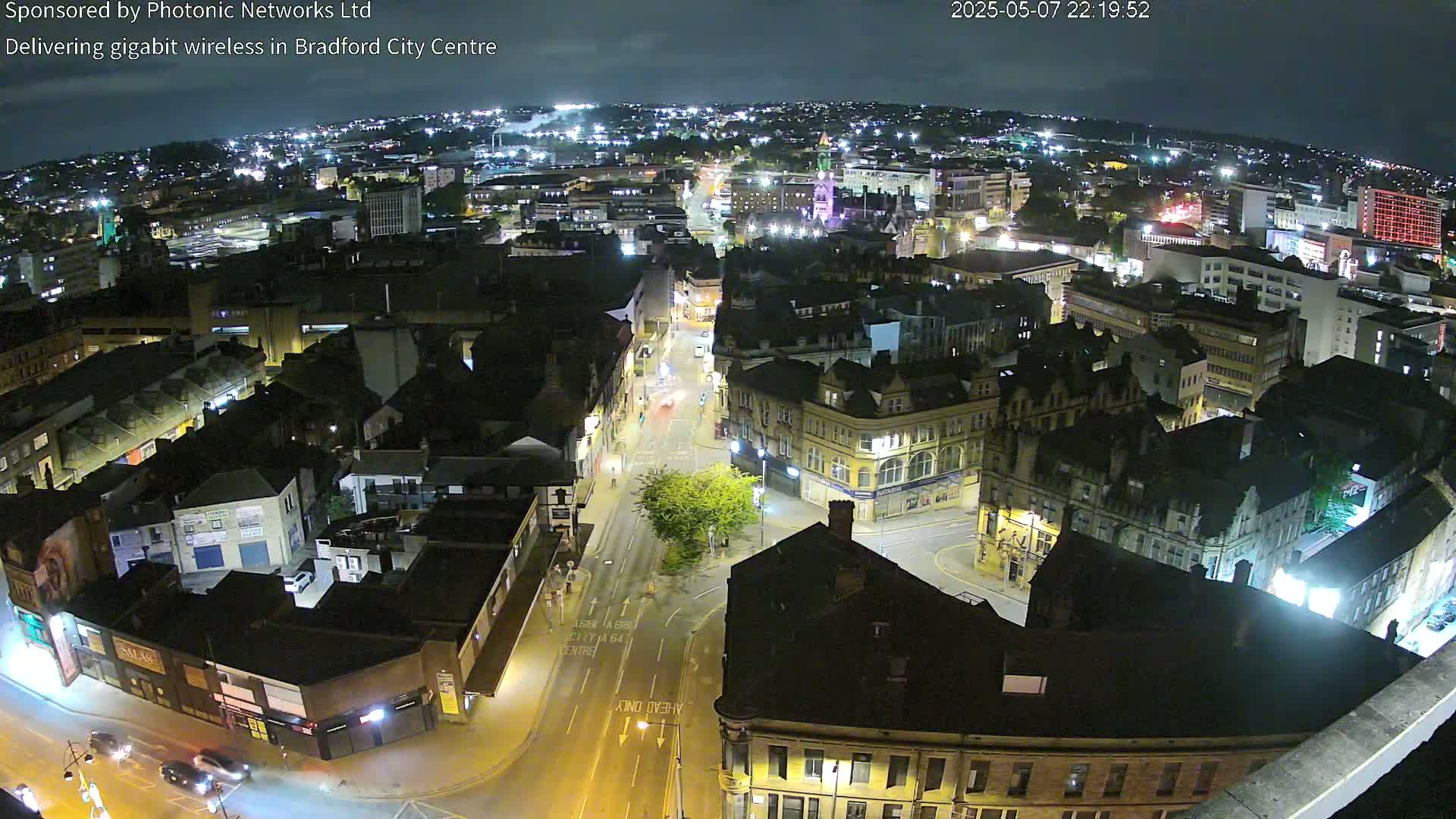 A nighttime, high-angle view of a city center with brightly lit buildings and streets, showing minimal traffic.