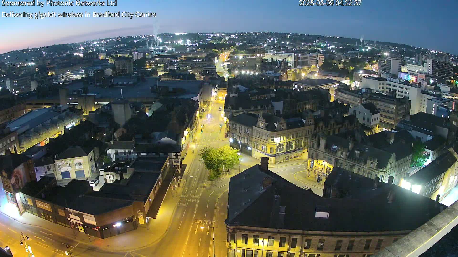 A nighttime, high-angle view of a city center with illuminated streets and buildings under a twilight sky.