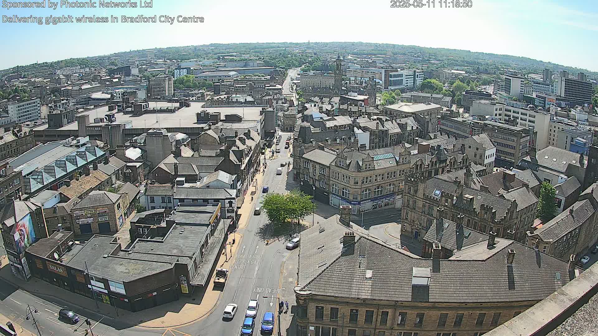A high-angle, sunny view of a city center with many buildings and a street with cars.