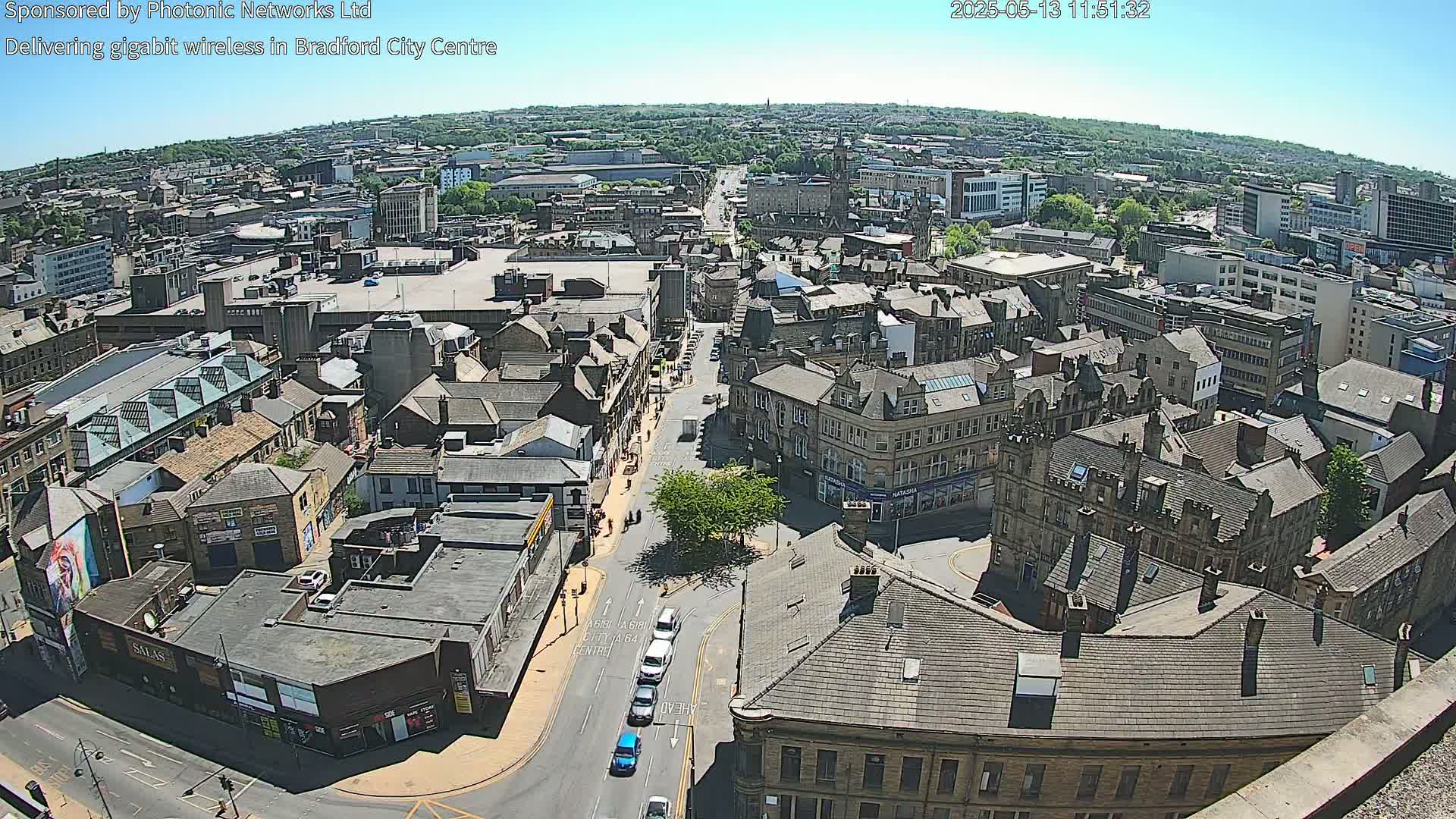 A high-angle, sunny view of a city center with many buildings and a few cars on the streets.