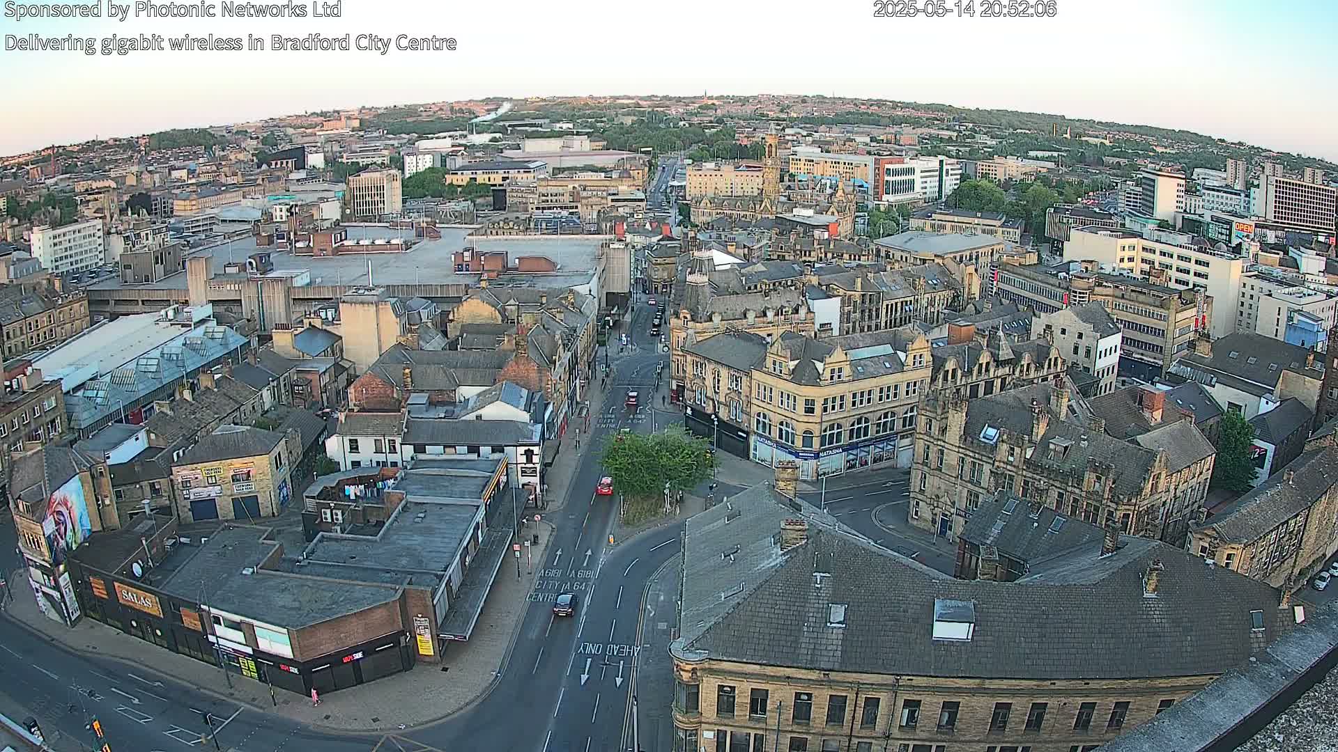 A high-angle, wide shot shows a city center at dusk, with many buildings and roads visible.