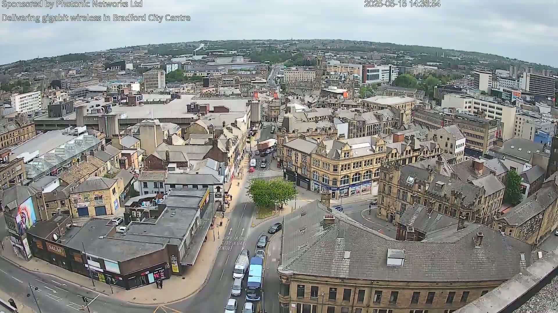 An aerial view of a city center on an overcast day shows many buildings and streets with cars and pedestrians.