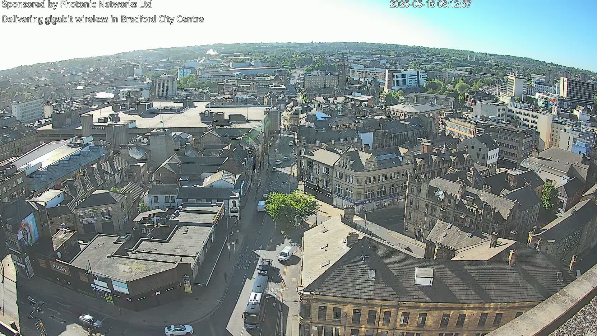 A high-angle, sunny view of a city center with many buildings and a few vehicles on the streets.