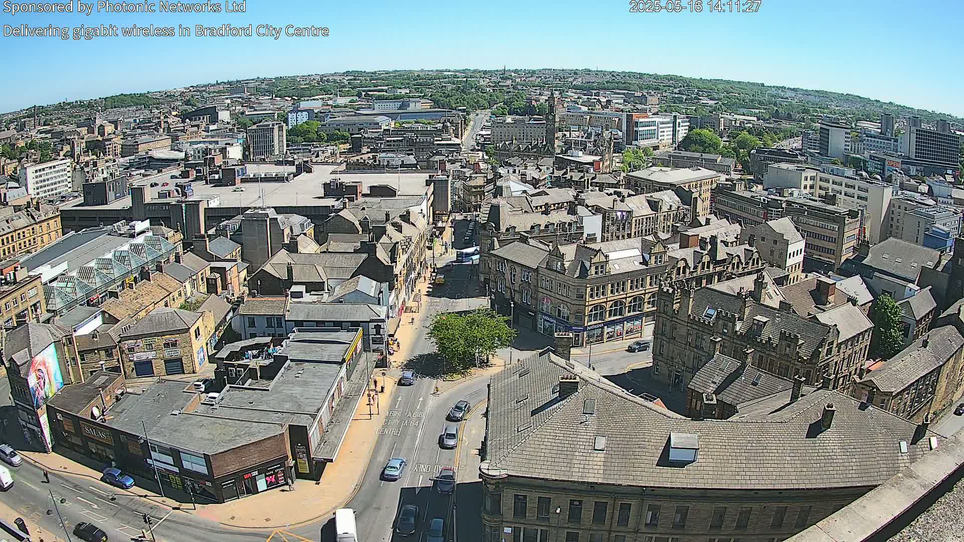 A high-angle, sunny view of a city center, showing numerous buildings and streets with sparse traffic.