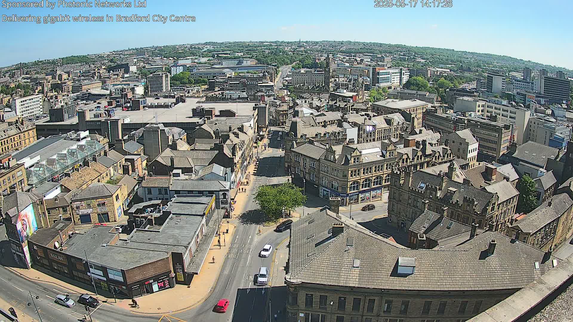 A high-angle, sunny view of a city's streets and buildings, showing several intersections and pedestrian traffic.