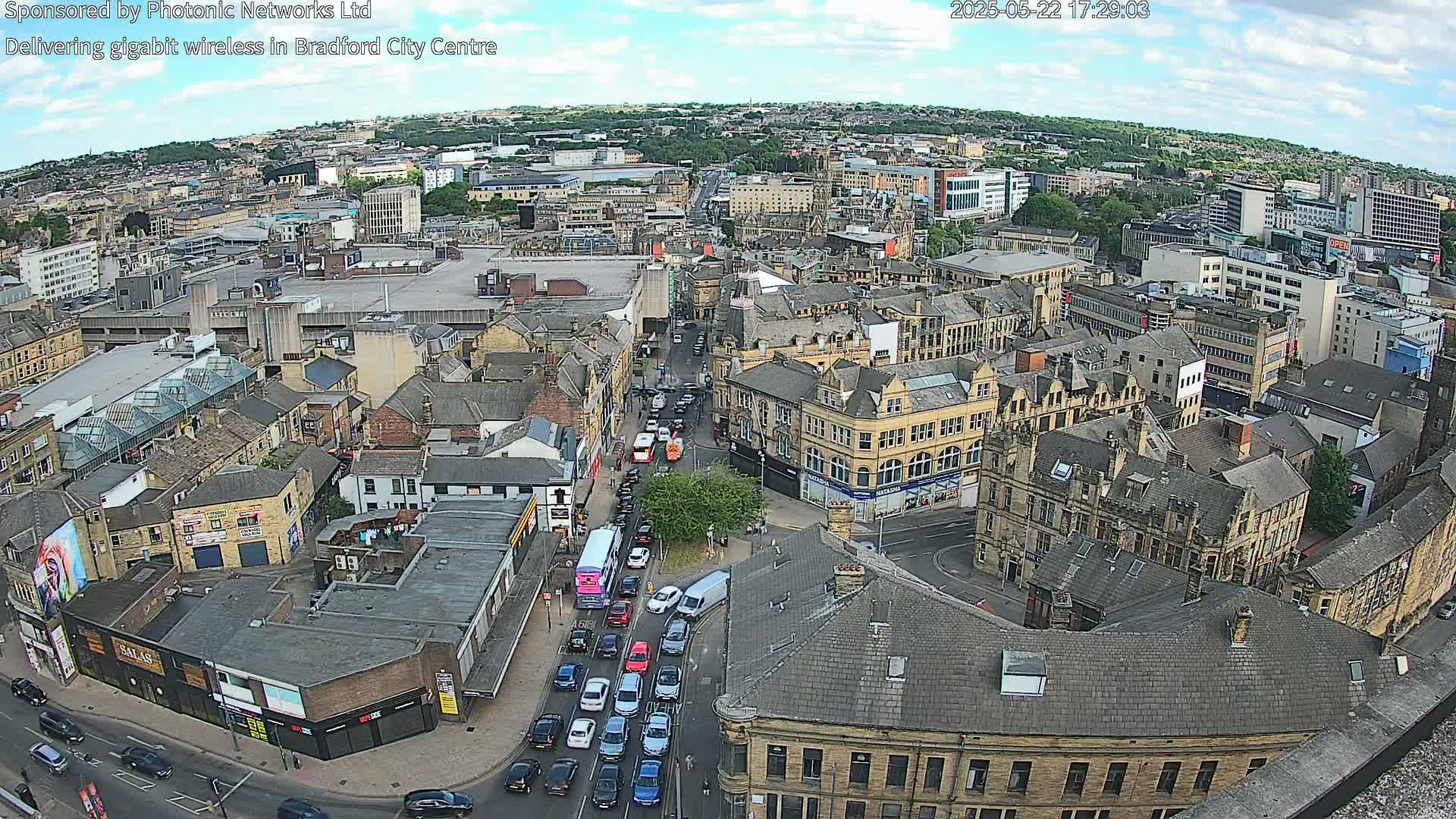 A high-angle, long shot of a city center on a partly sunny day, showing numerous buildings and congested traffic on a street below.