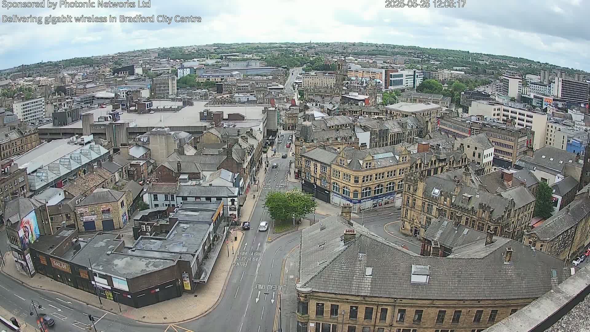 A high-angle, wide shot of a city center on an overcast day shows many buildings and streets, with cars visible on the roads.
