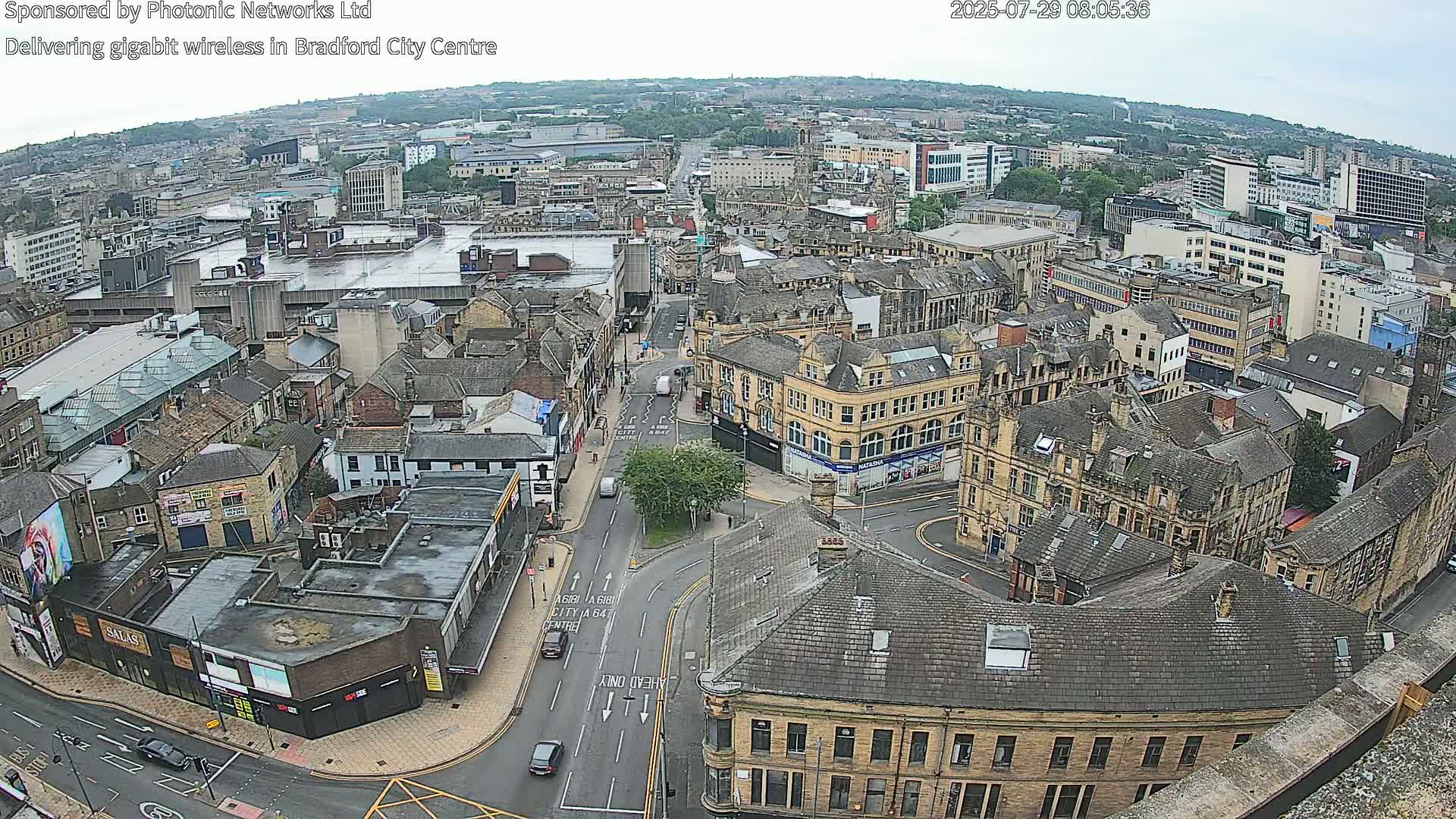 An aerial view of a city center on an overcast day, showing a network of streets, buildings, and vehicles.
