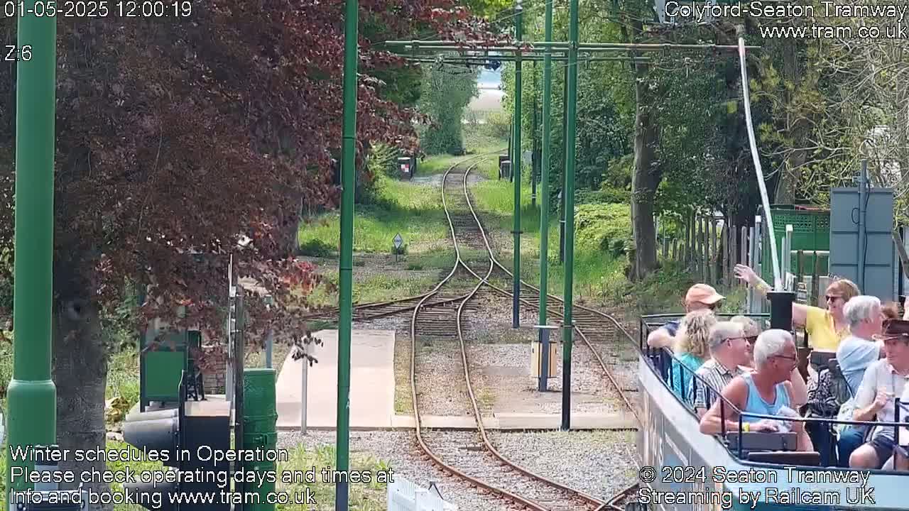 A sunny day at a railway junction where two sets of tracks meet, with a tram full of passengers approaching.