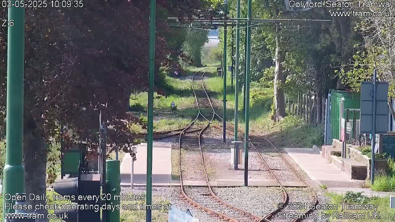 A sunny view of a tram track splitting into two lines, surrounded by green vegetation and trees.