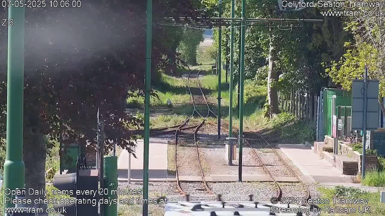 A sunny view of a tram line splitting into two tracks, surrounded by green trees and grass.