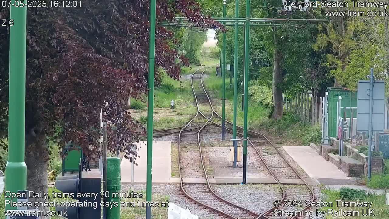 Tram tracks split into two diverging lines, surrounded by green vegetation under a partly cloudy sky.