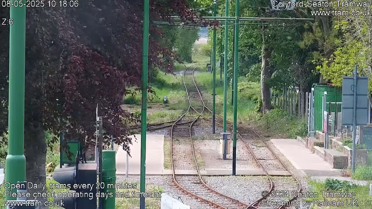 A view down a railway track splitting into two, surrounded by greenery under a mostly sunny sky.