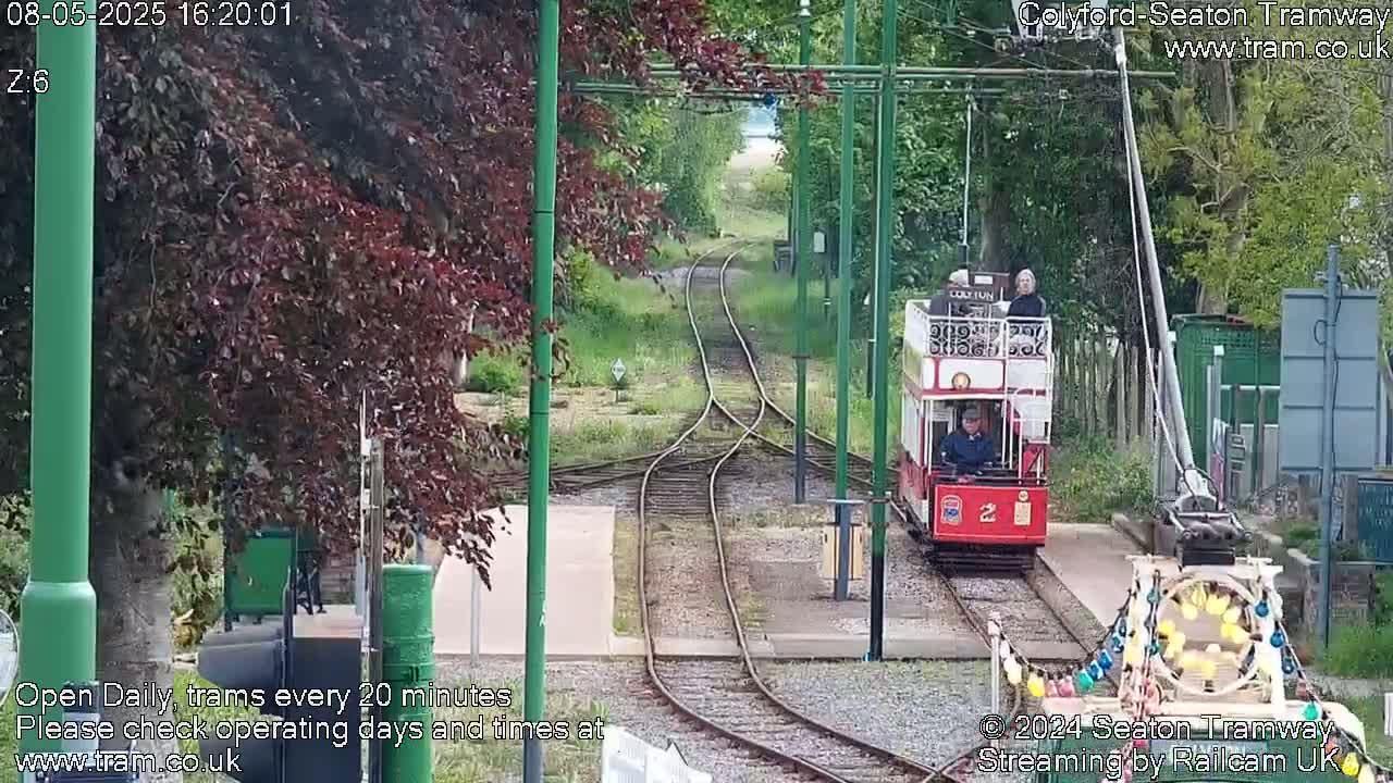 A red tram approaches a railway junction on a partly sunny day.