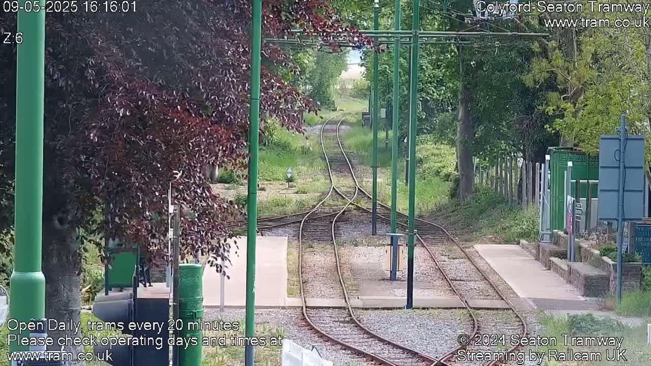 A view down a split set of train tracks through a tree-lined area on a partly sunny day.