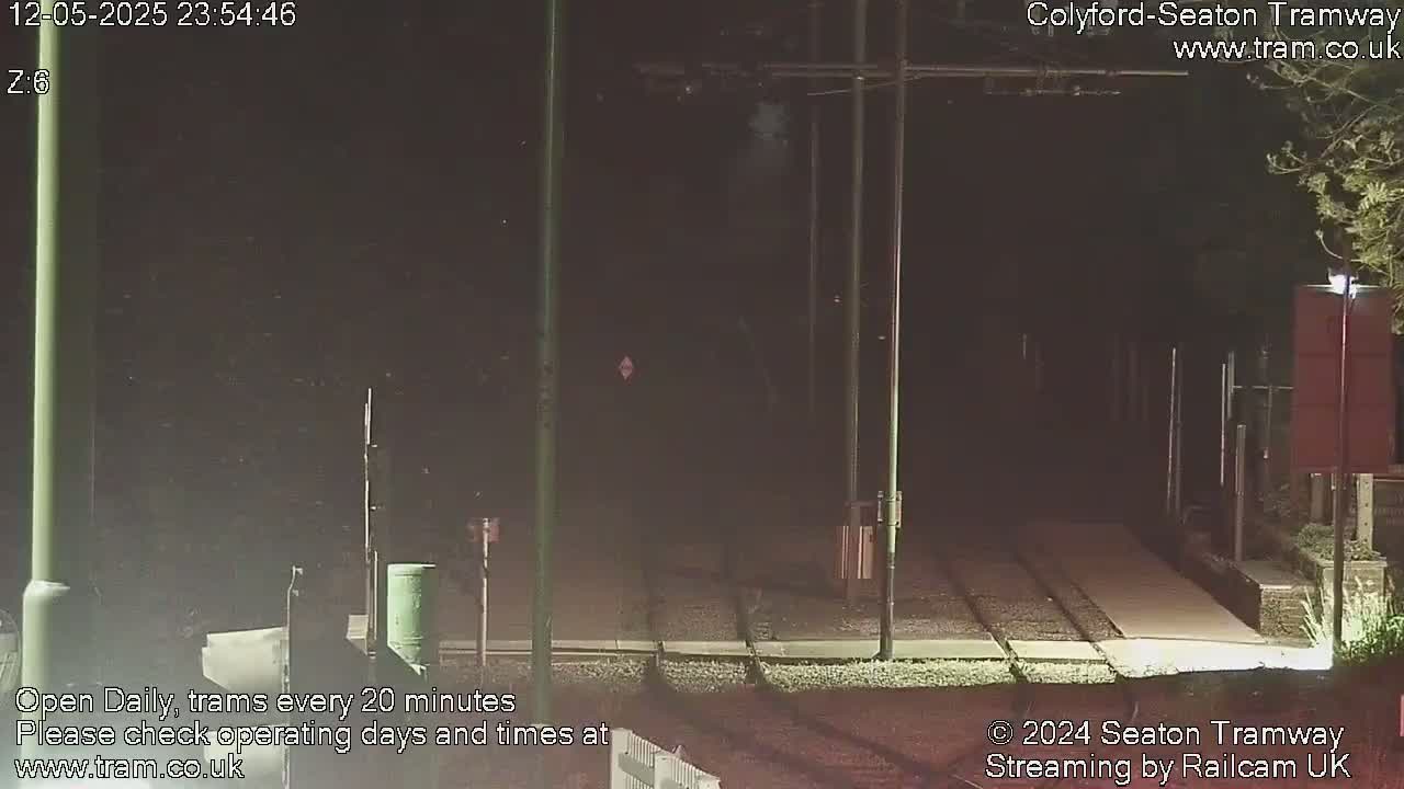 A nighttime view of a tram track, with overhead wires and poles, under a dark sky.