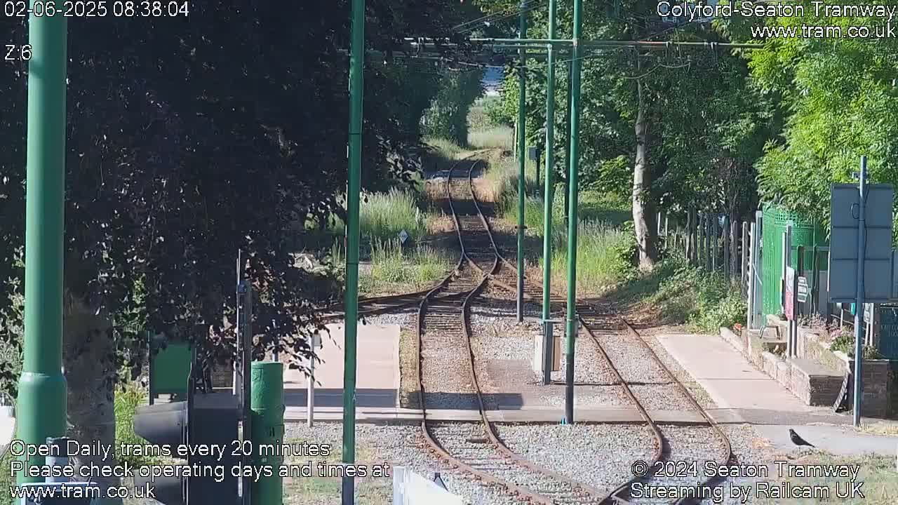 A sunny view of a tram railway track splitting into two directions, surrounded by green trees and vegetation.