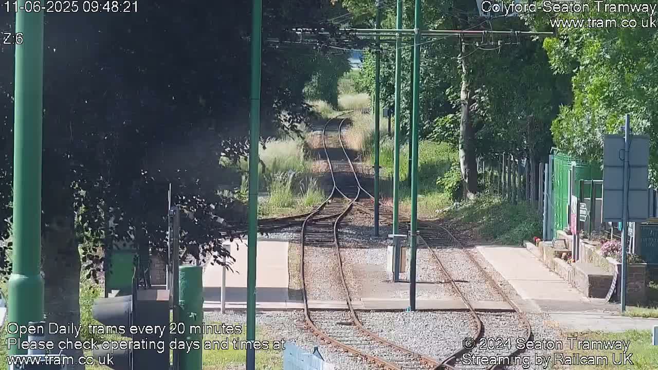 A sunny day at a railway station with train tracks branching off into a tree-lined area.
