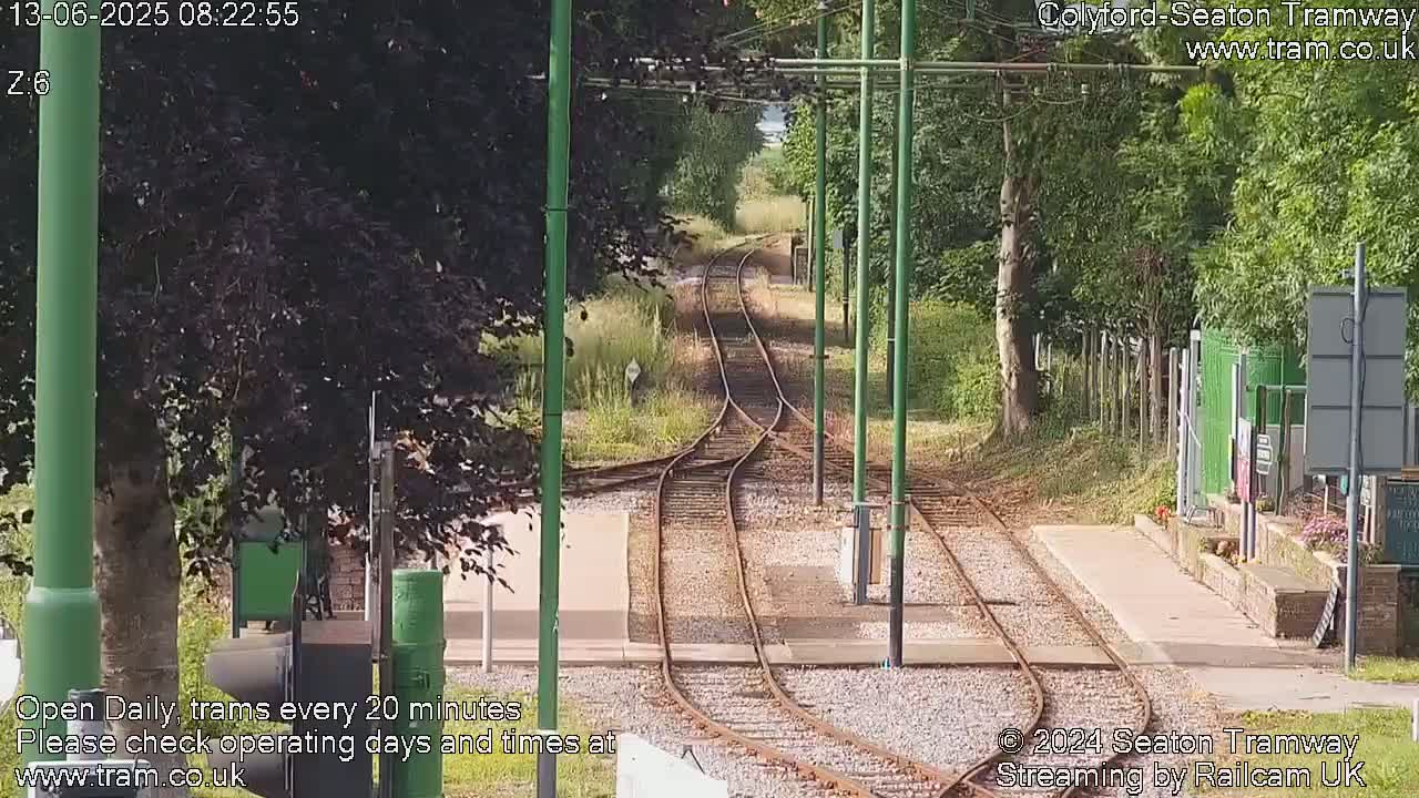 A sunny view of a train track splitting into two diverging paths, surrounded by trees and greenery.