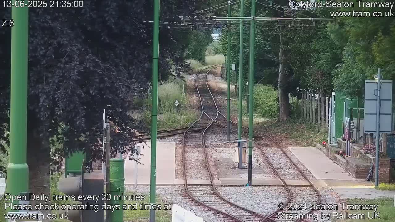Tram tracks curve through a tree-lined area on a partly sunny day.