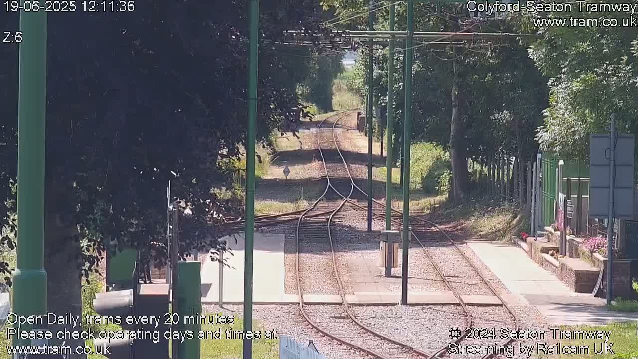 A sunny outdoor view of a tram track splitting into two directions, lined with trees and bordered by a paved walkway.