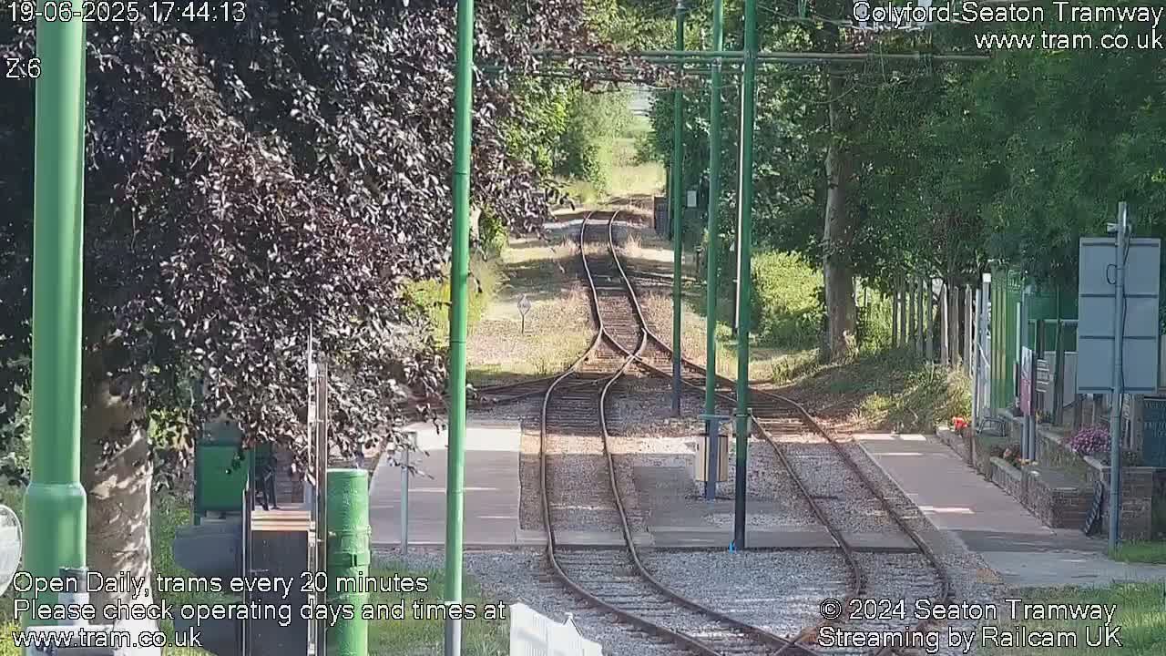 A sunny view of a train track splitting into two directions, lined with trees and greenery.