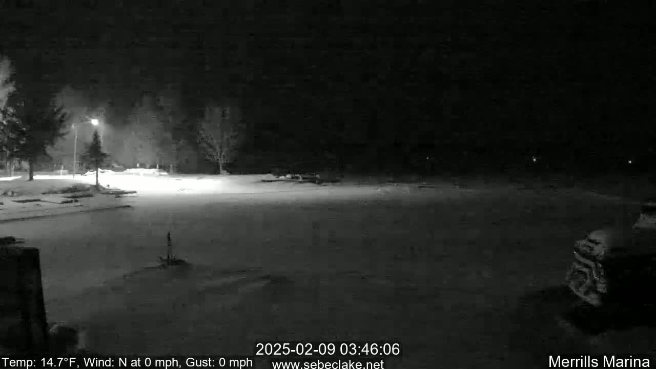 A snow-covered parking lot is dimly lit at night under a dark sky.