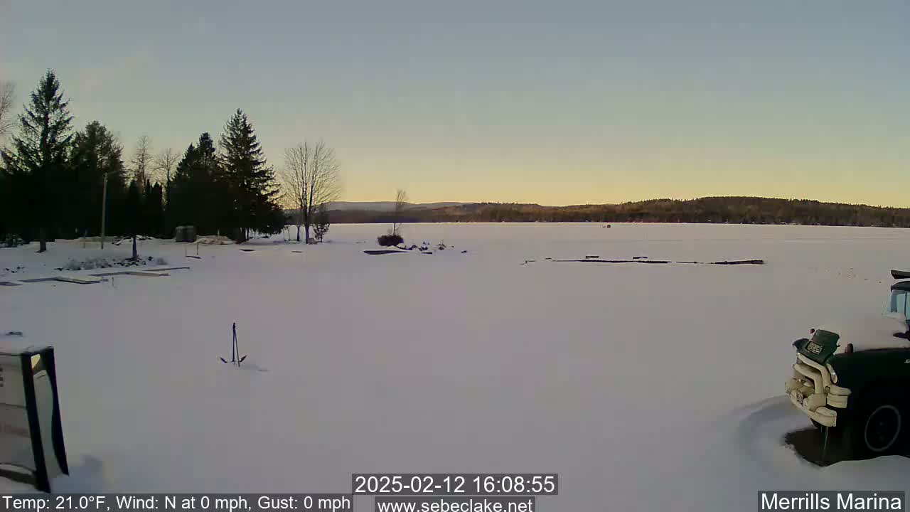 A snow-covered frozen lake is visible, with a calm sky and a line of dark evergreens in the background.