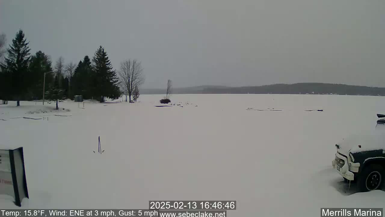 A snow-covered shoreline with a frozen lake in the background under an overcast sky.