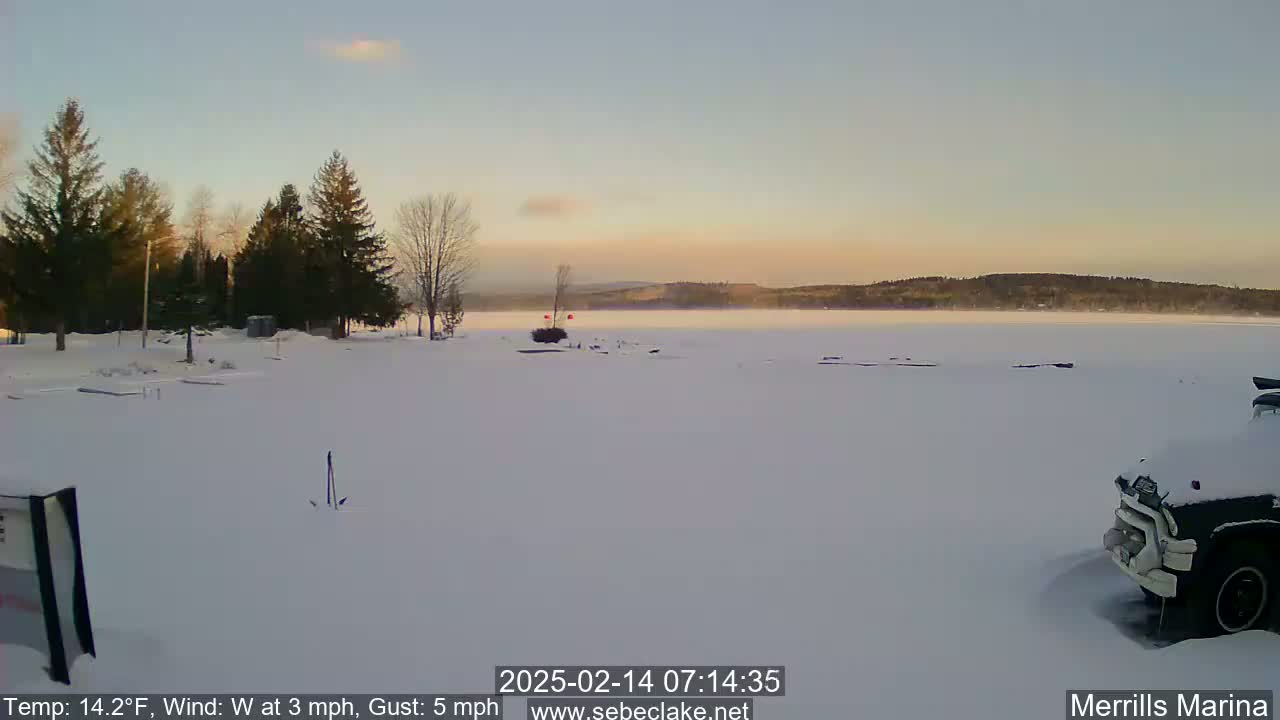 A snow-covered marina overlooks a frozen lake under a pale sunrise.