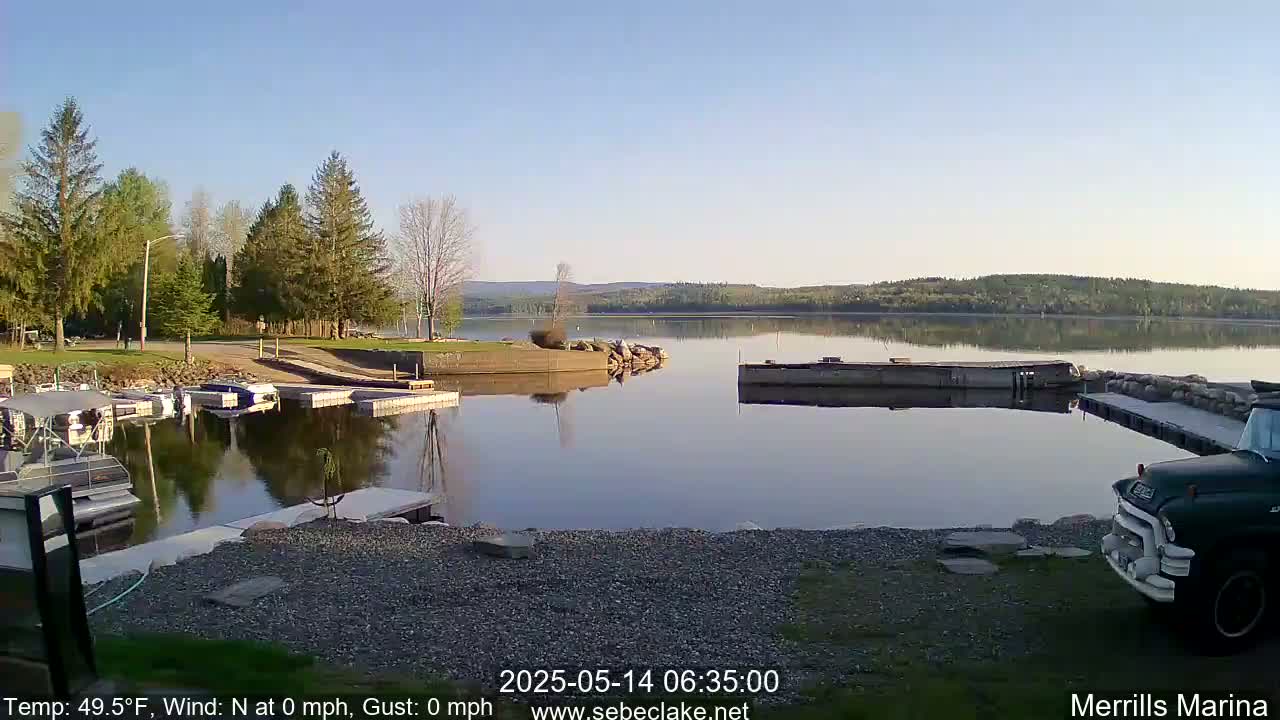 A calm lake with a marina, boats, and a truck parked by the shore under a clear, sunny sky.