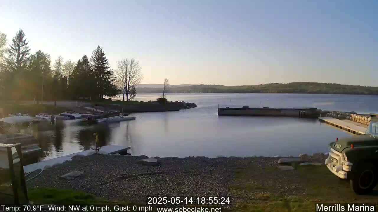 A calm lake at sunset with boats docked at a marina, and a truck parked on the shore.