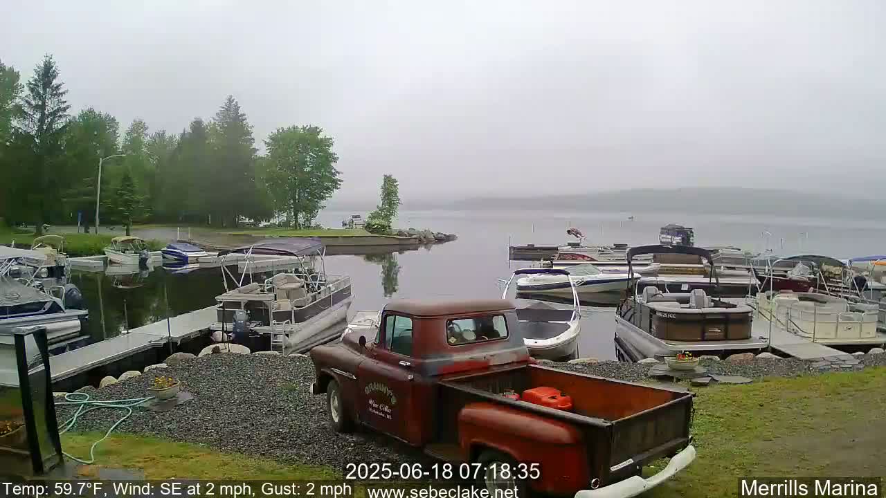 A foggy morning reveals numerous boats docked at a marina, with a vintage red pickup truck parked nearby.